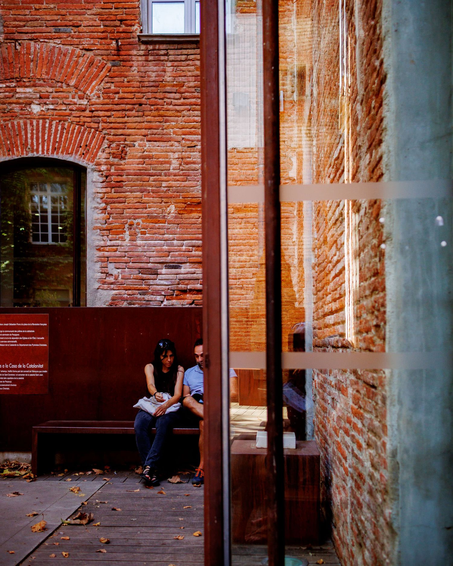Two people sitting on bench between historic red brick walls at Perpignan venue.