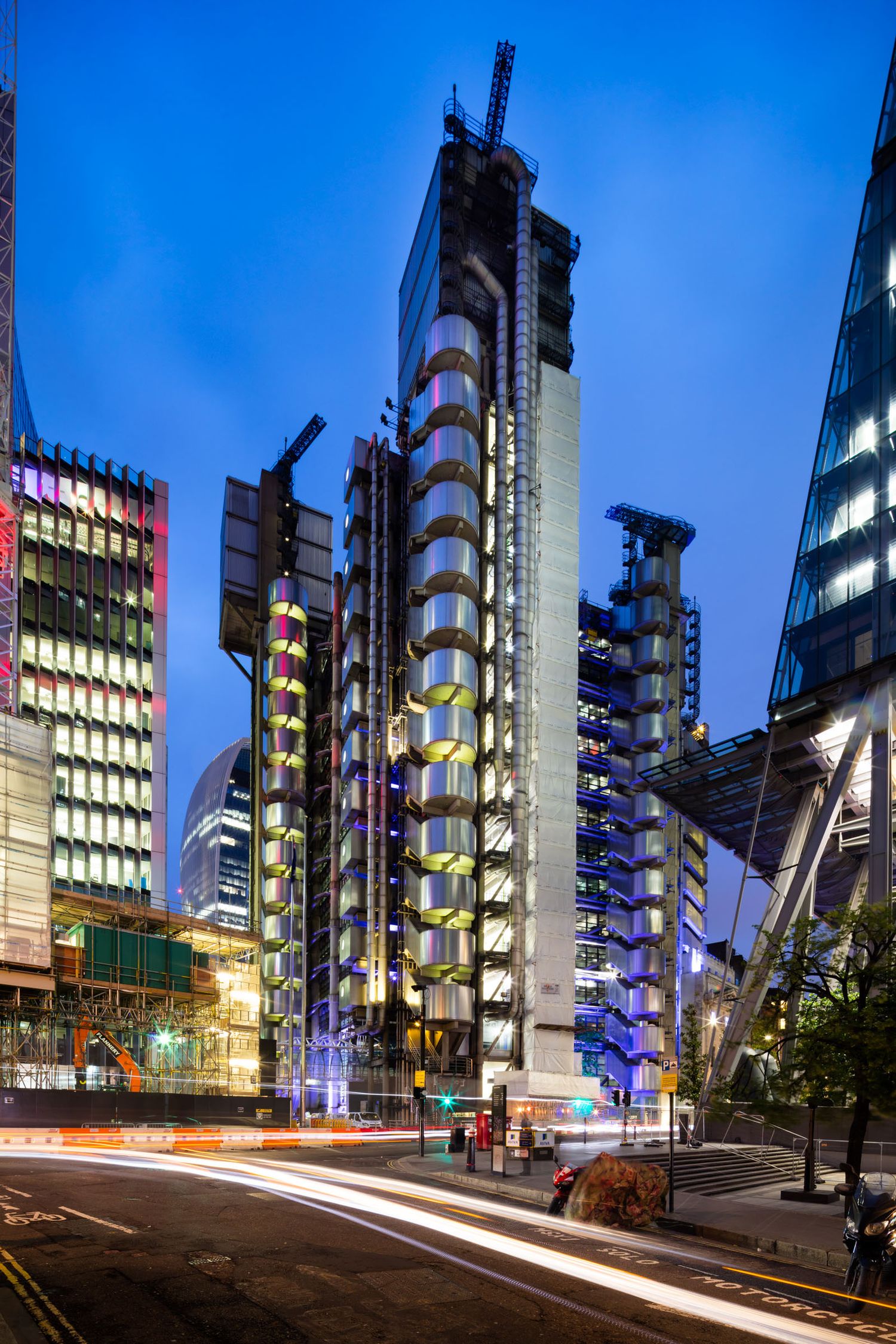Night cityscape of the iconic Lloyd's of London building with light trails from passing traffic on wet streets.