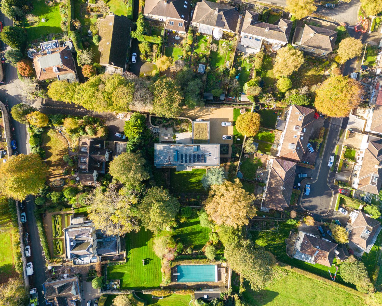Aerial drone view of suburban residential neighborhood with gardens, trees and swimming pool in autumn.