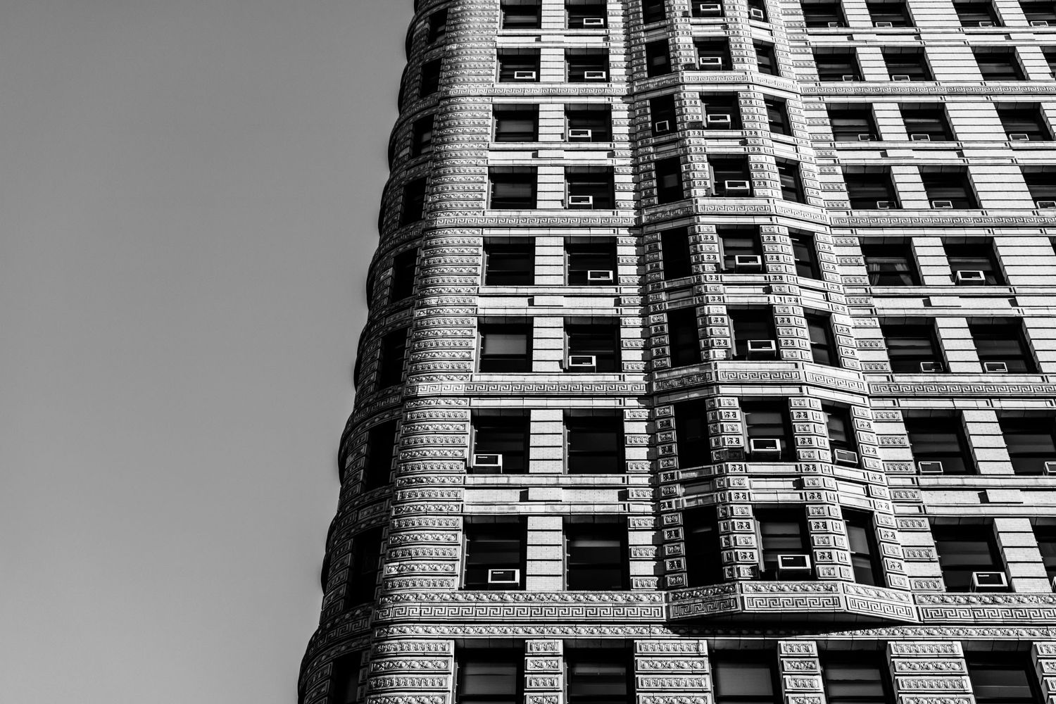 Black and white photo of a curved Art Deco skyscraper facade with rows of windows against a gray sky.
