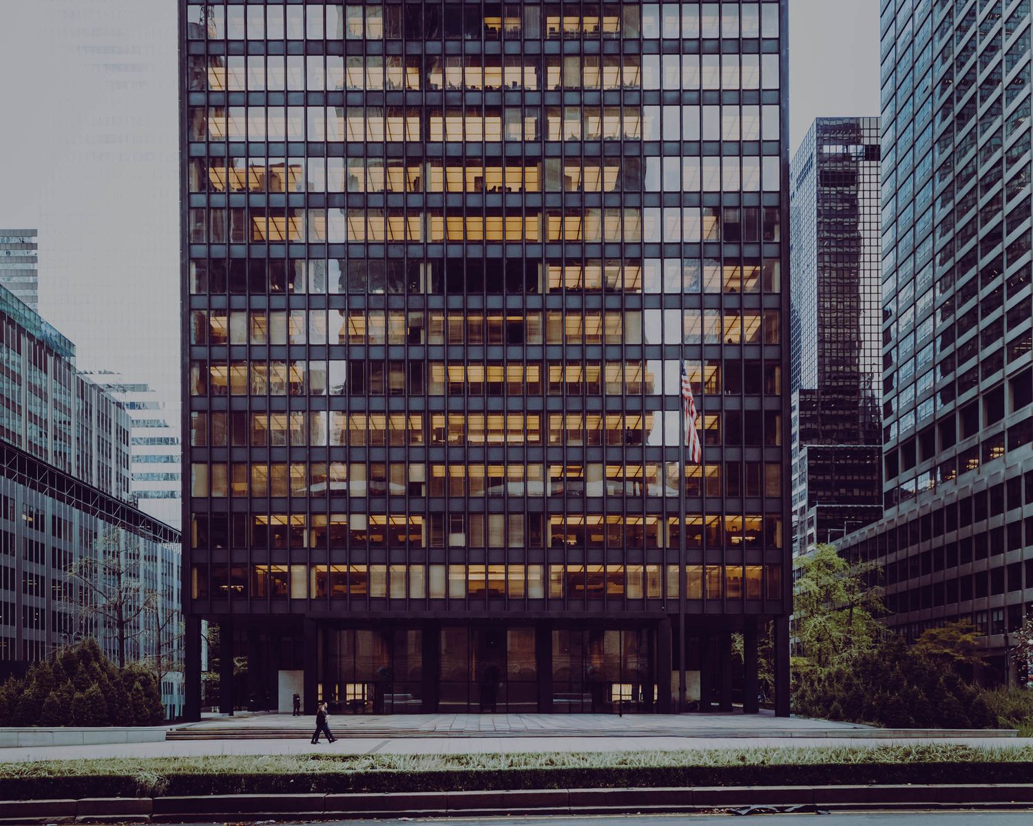 Modern glass office skyscraper with illuminated windows in an urban cityscape.