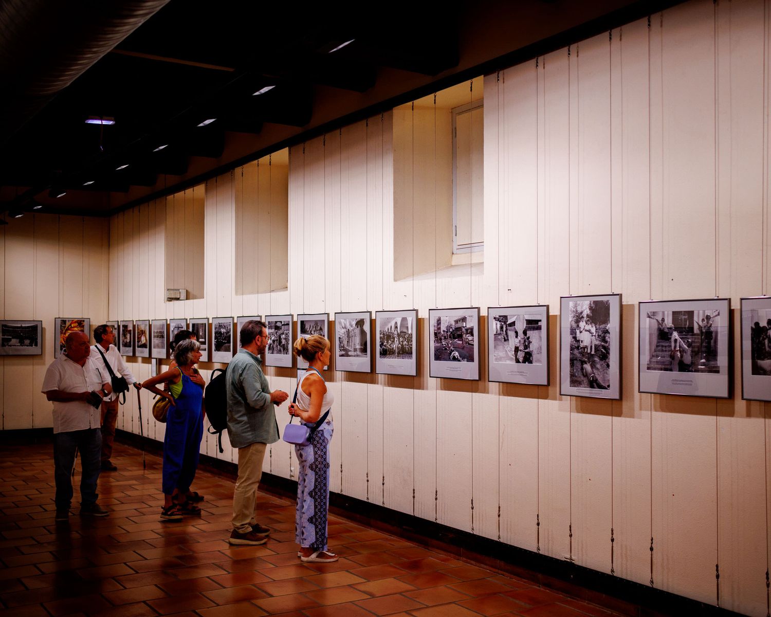 Visitors examining black and white framed photographs along gallery wall at photo festival.