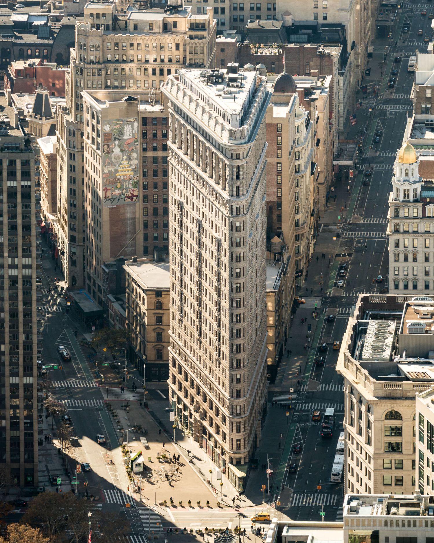Aerial view of the iconic Flatiron Building in New York City, surrounded by urban streets and skyscrapers.