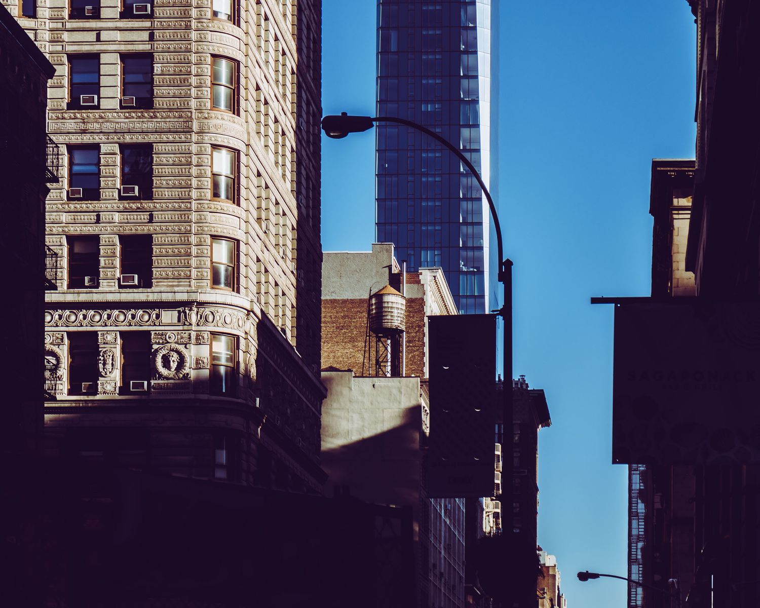 Urban cityscape featuring classic brick buildings and a modern glass skyscraper under a clear blue sky.