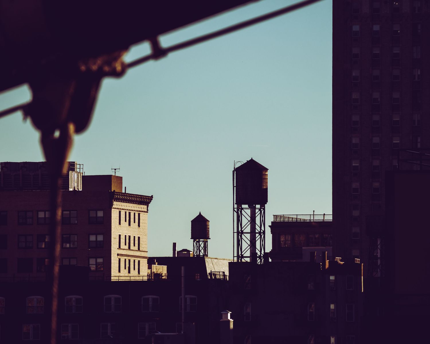 Silhouetted city skyline at dusk featuring iconic water towers atop rooftops against a clear blue sky.