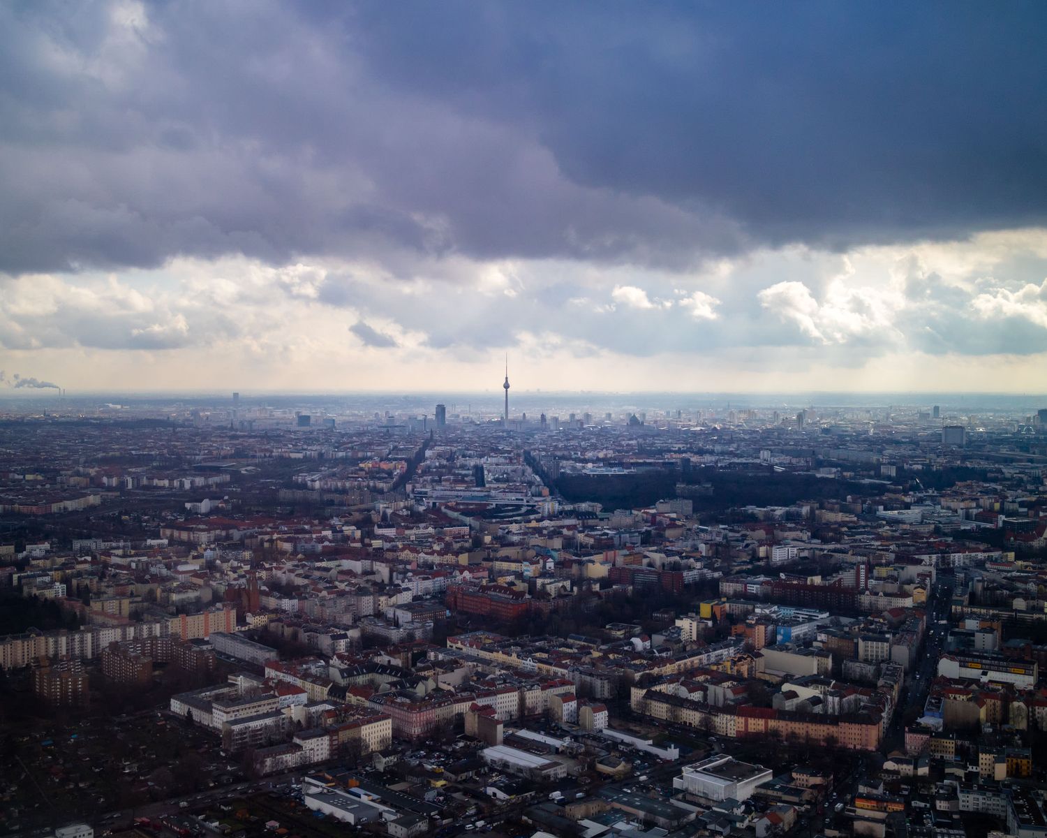 Dramatic aerial view of Berlin cityscape with TV tower on the horizon under moody storm clouds at dusk.