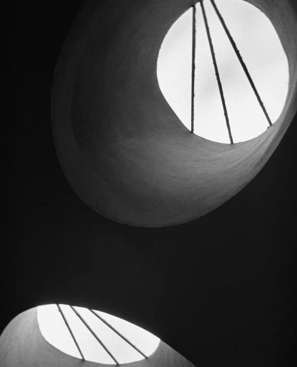 Black and white architectural photo of two circular skylights with metal cables casting dramatic shadows.