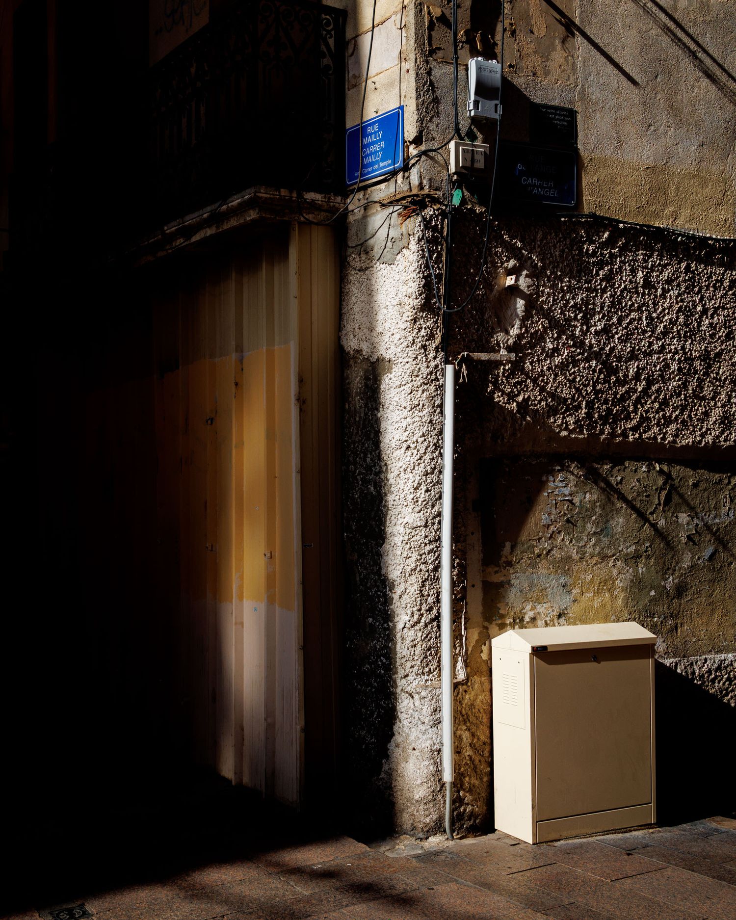 Sunlit stone building corner with blue street sign, curtained doorway, and beige utility box.