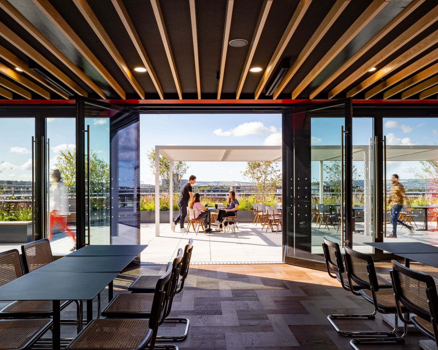 Modern office space with open glass walls leading to a rooftop terrace with city views.
