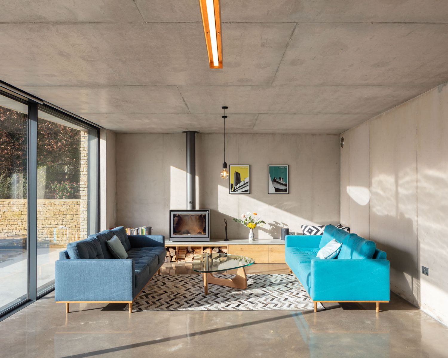 Contemporary concrete living room with blue sofas, patterned rug and suspended fireplace.