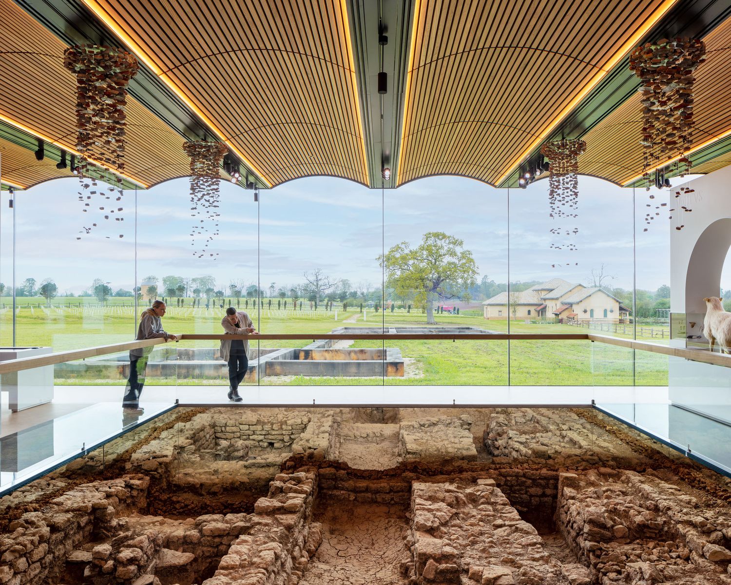 Museum interior showcasing ancient Roman ruins beneath a scalloped wooden ceiling with panoramic countryside views.