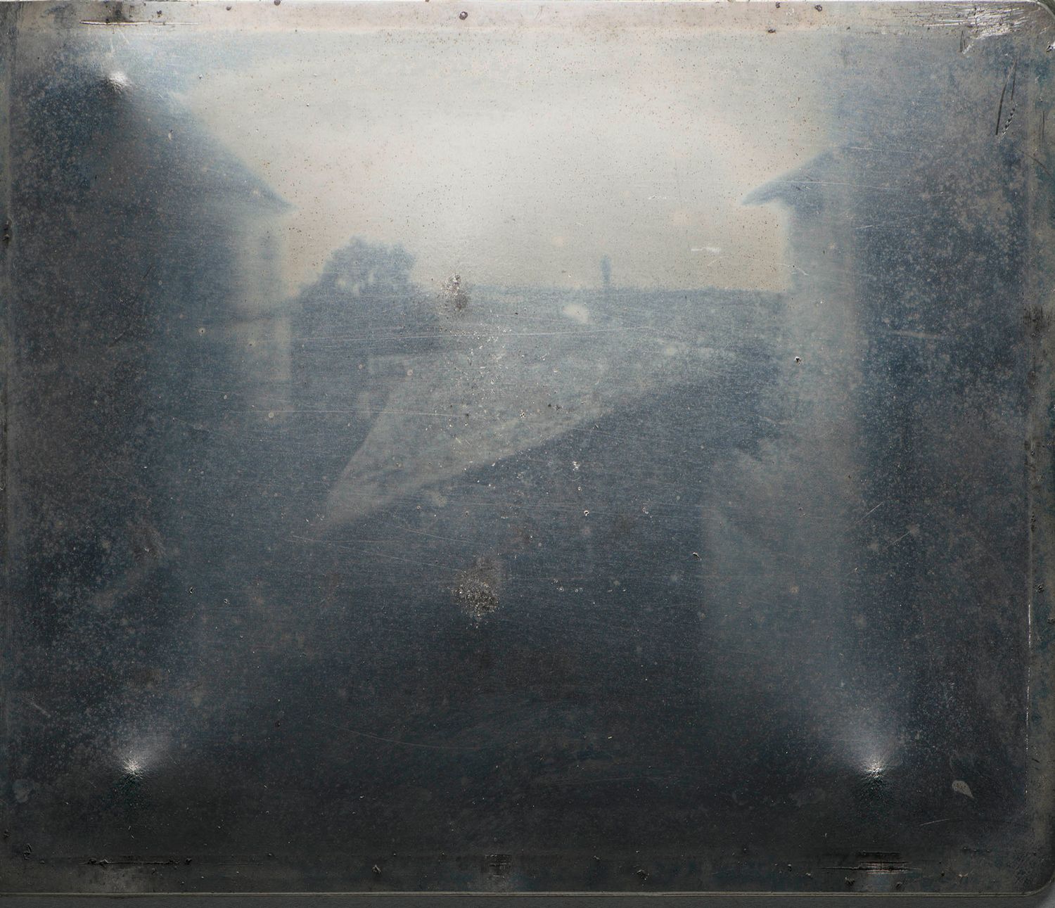 Early daguerreotype photograph showing a misty rooftop cityscape viewed between two dark building facades.