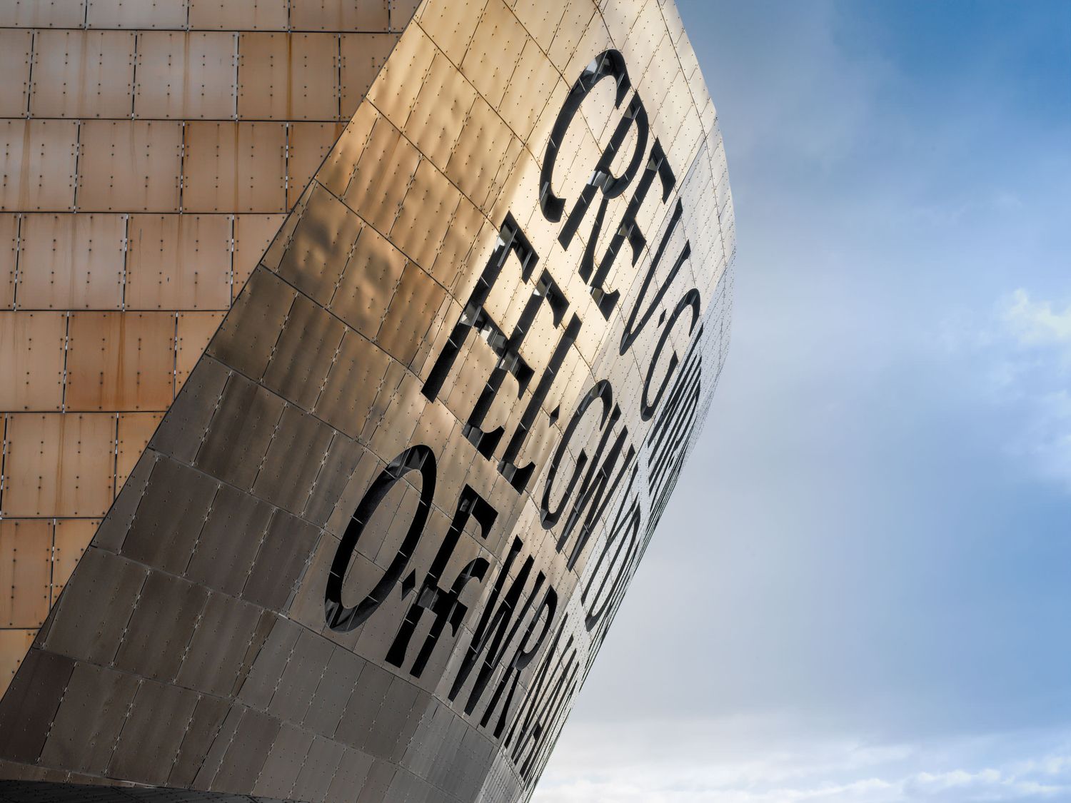 Close-up of the Wales Millennium Centre facade with Welsh text inscription against blue sky.