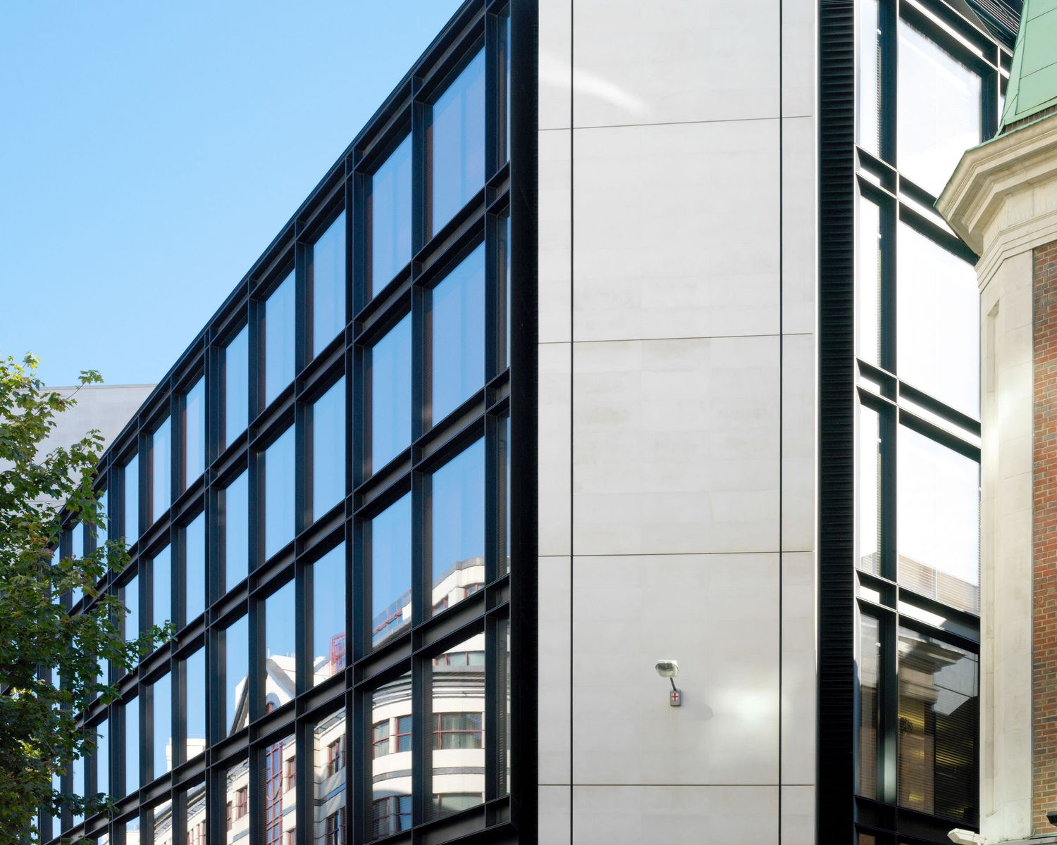Close-up of a contemporary glass curtain wall building facade with black framing against a bright blue sky.