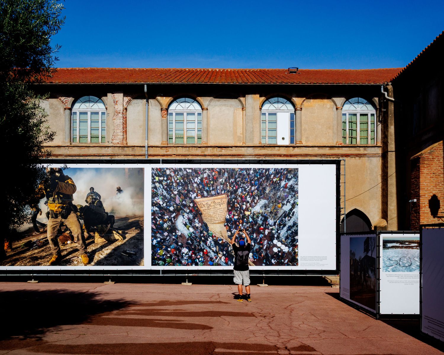 Person viewing large outdoor photojournalism prints mounted on a historic building facade.