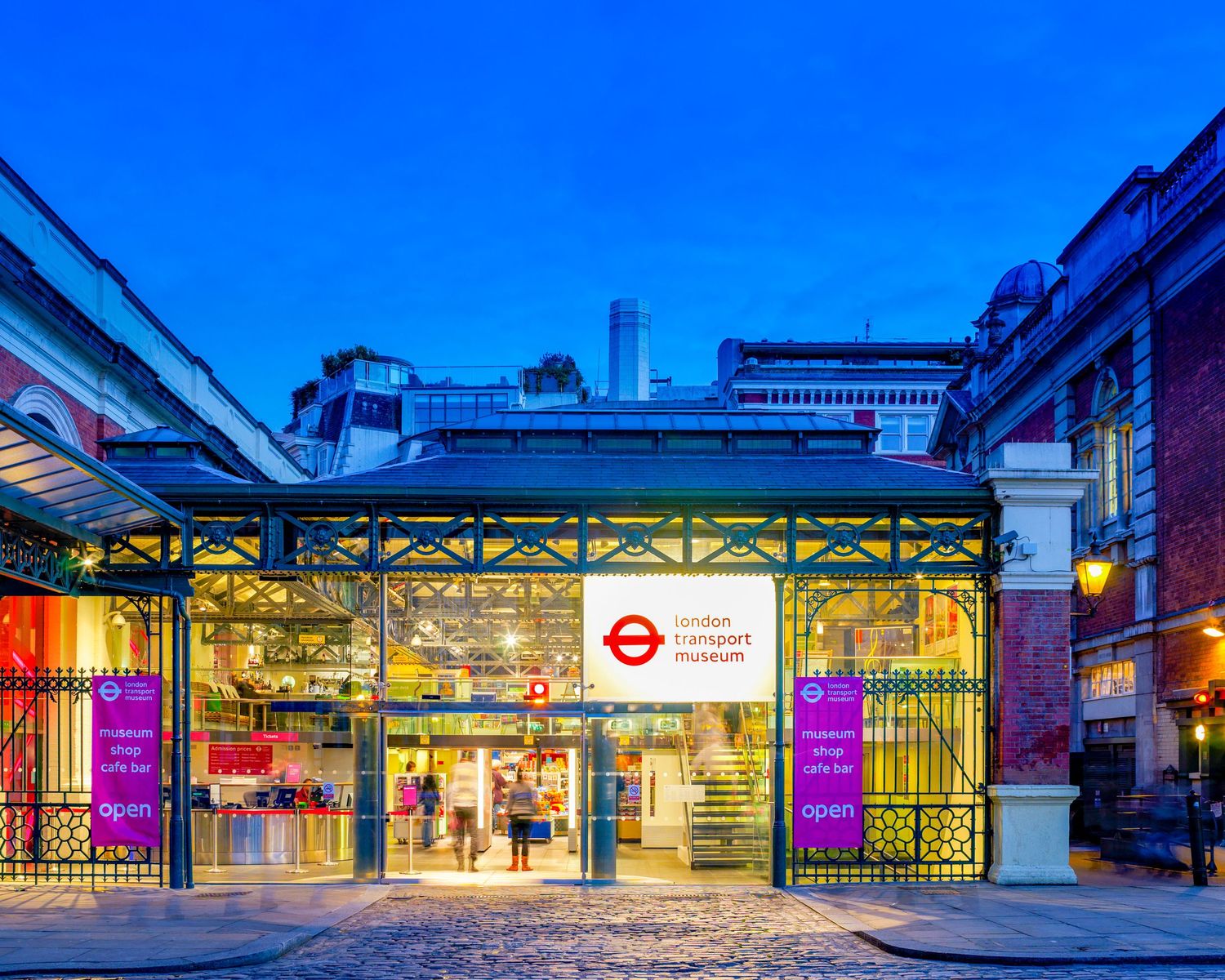 London Transport Museum entrance at dusk with illuminated glass facade and iconic red roundel sign in Covent Garden.