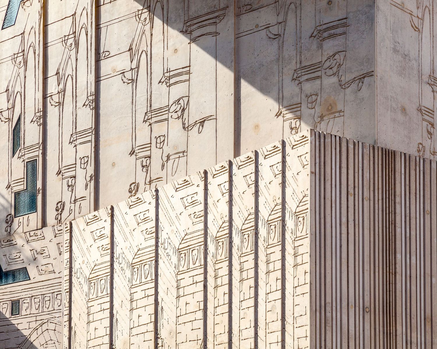 Close-up of an ornate building facade with intricate carved reliefs and vertical stone columns in warm sunlight.