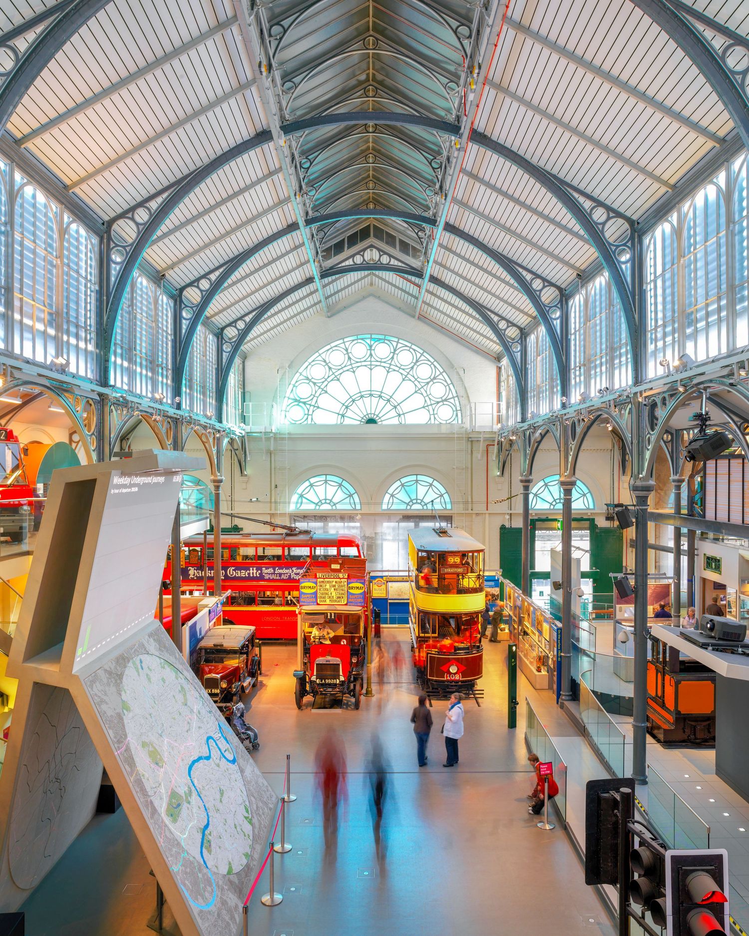 Interior view of London Transport Museum featuring vintage buses and trams displayed under a grand Victorian iron and glass roof.