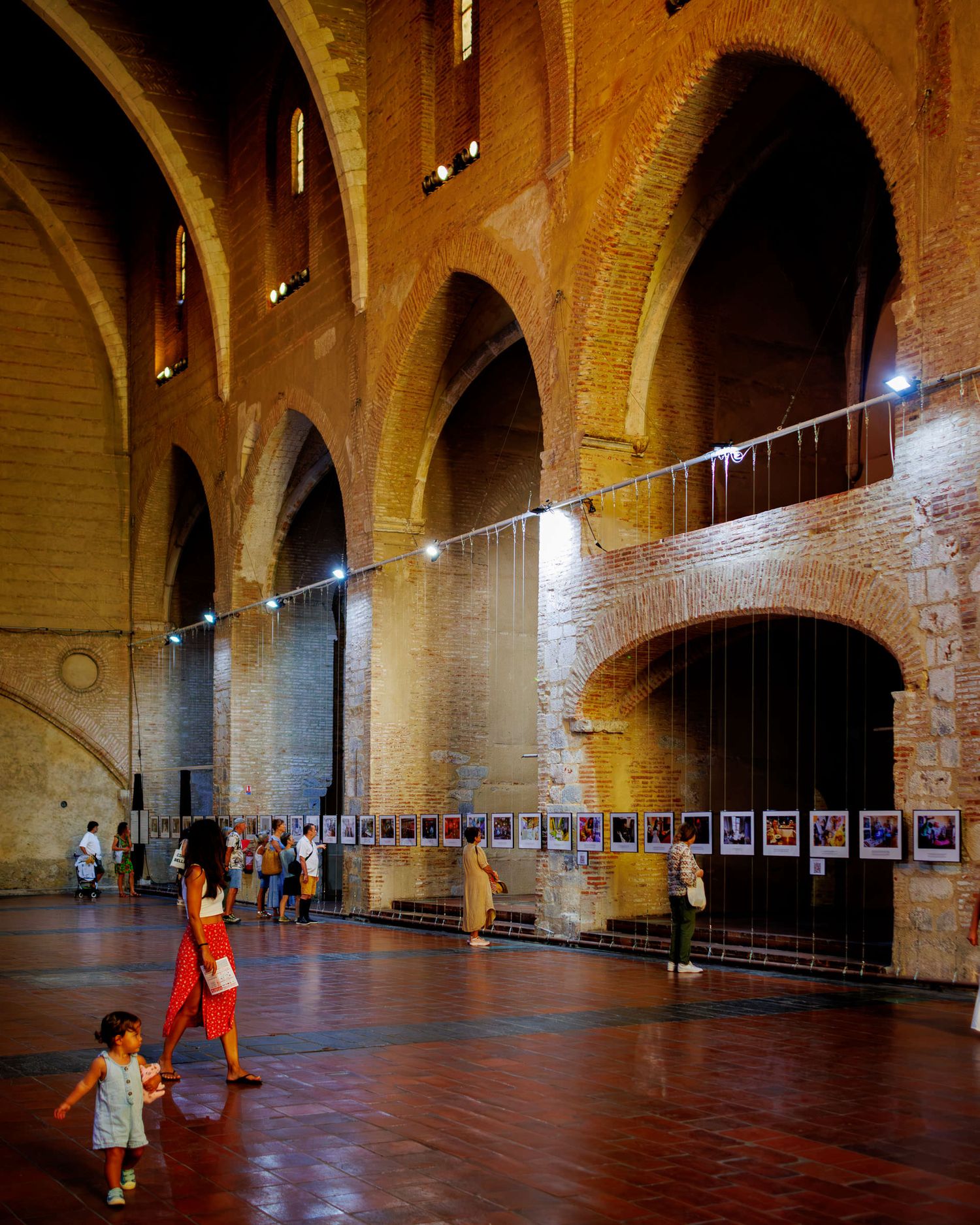 Visitors walking through a grand medieval brick hall with arched ceilings displaying a photography exhibition.