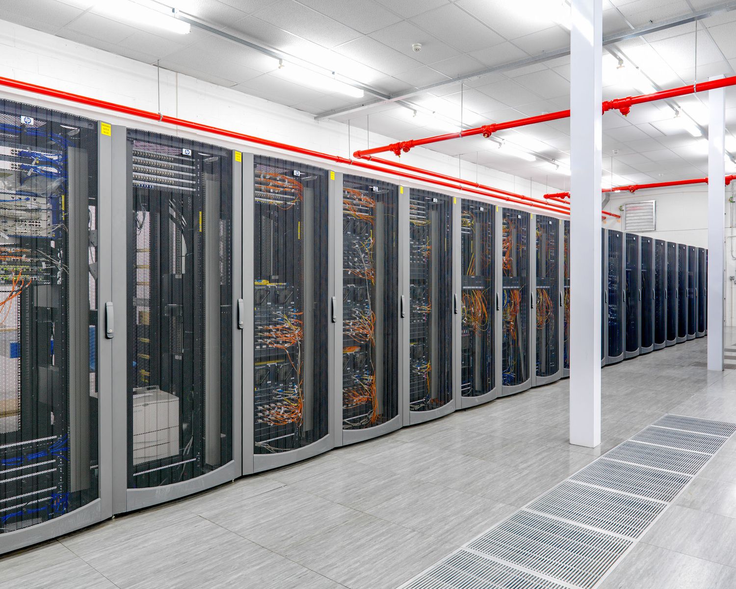 Modern data center server room with rows of network equipment racks and colorful cables in a white facility.