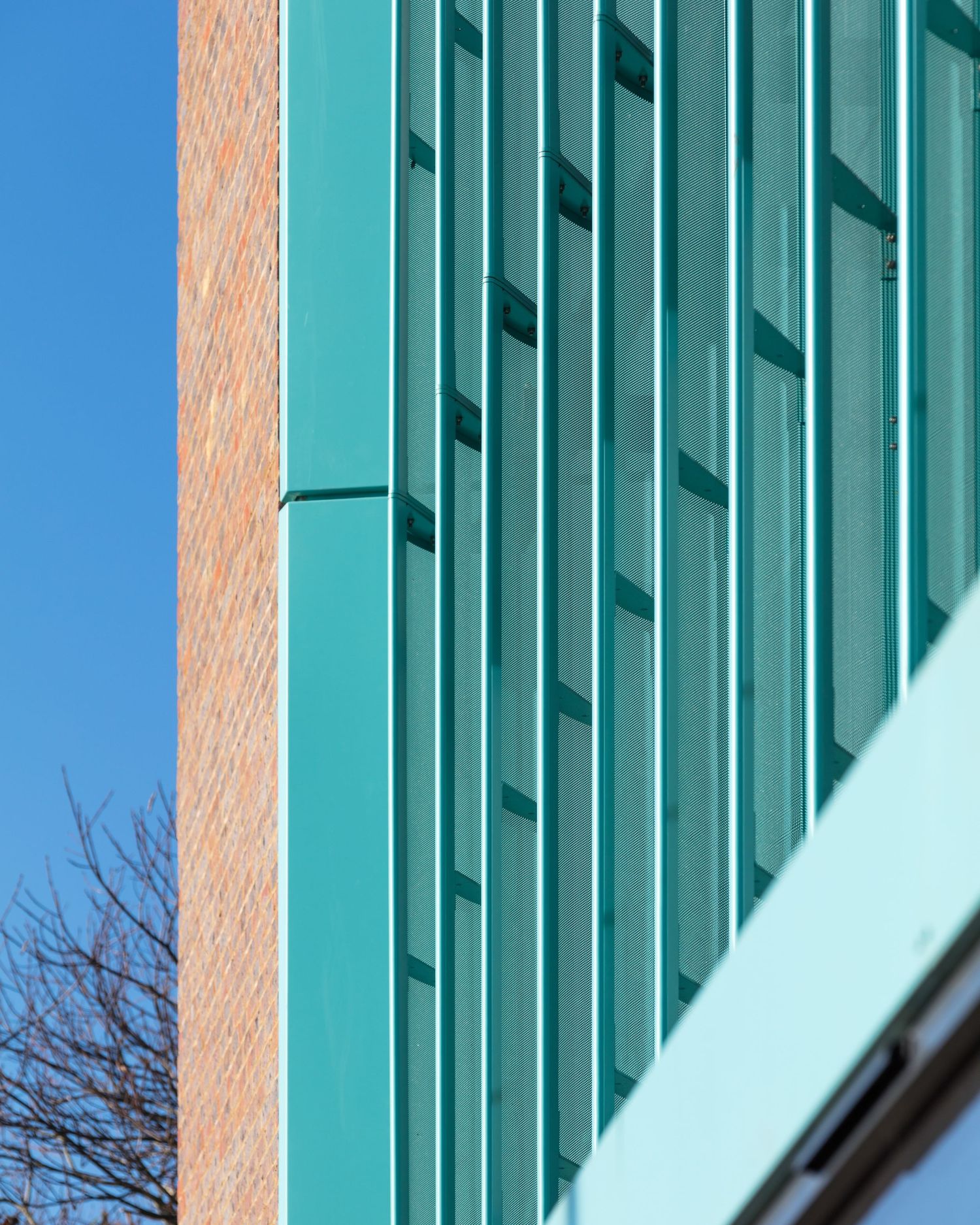Modern building facade with teal green metal panels beside a red brick wall against a clear blue sky.