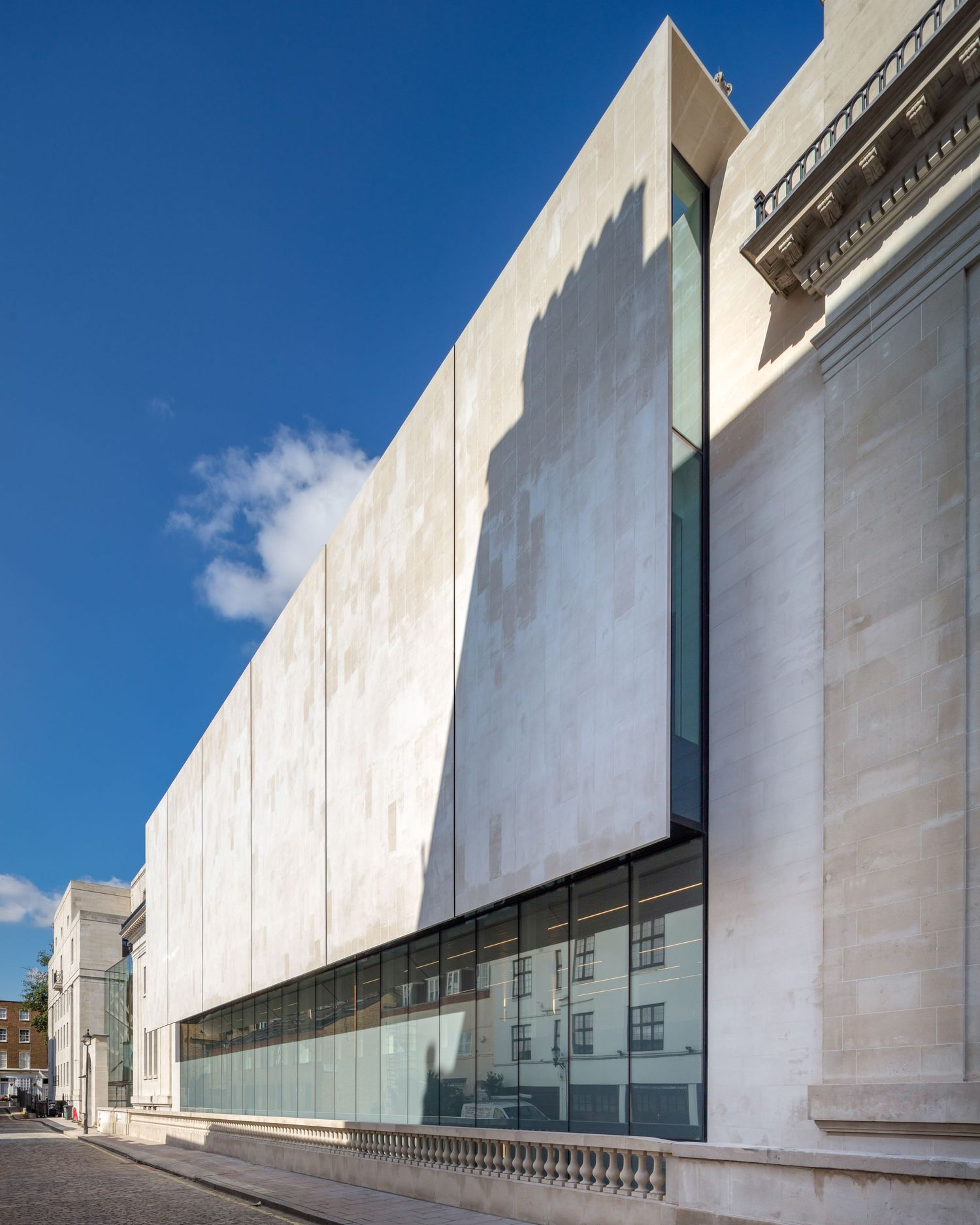 Modern white stone museum facade with floor-to-ceiling glass windows under a bright blue sky in London.