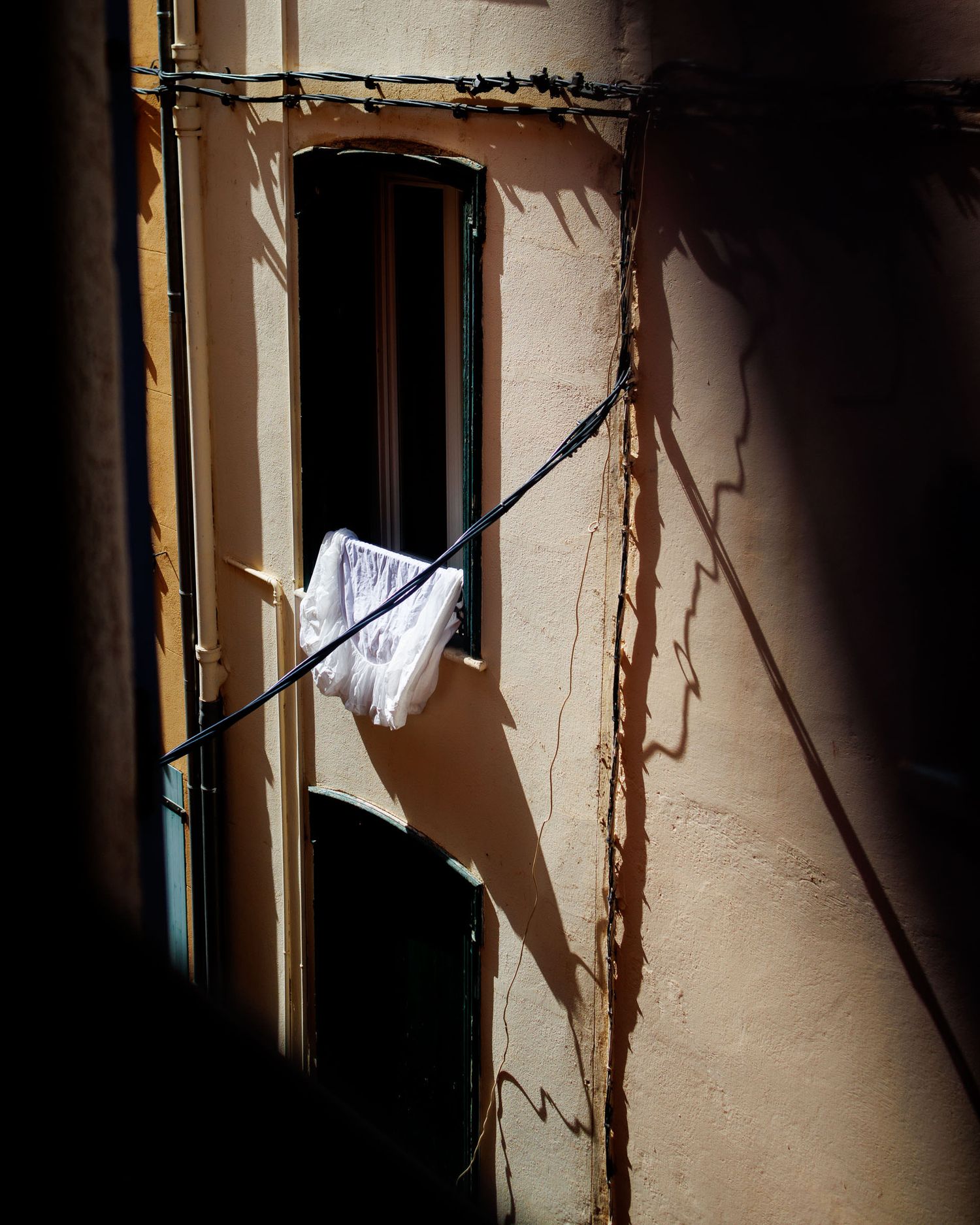 White garment hanging on a wire outside a weathered building window with dramatic shadows on the wall.