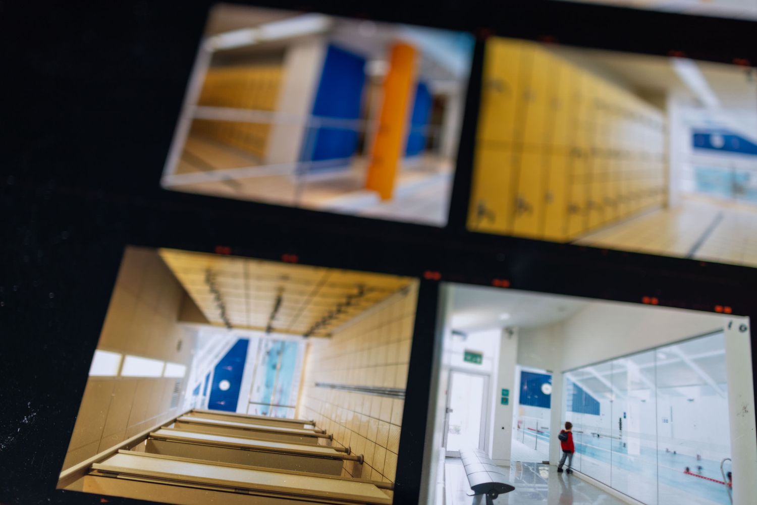 Multiple security monitor screens displaying school hallways, colorful lockers, staircases, and corridors in an educational facility.