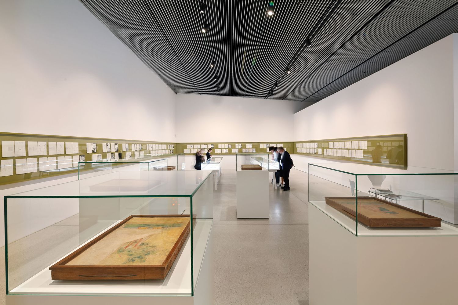 Modern museum gallery displaying Asian artifacts in glass cases with framed artwork along white walls.