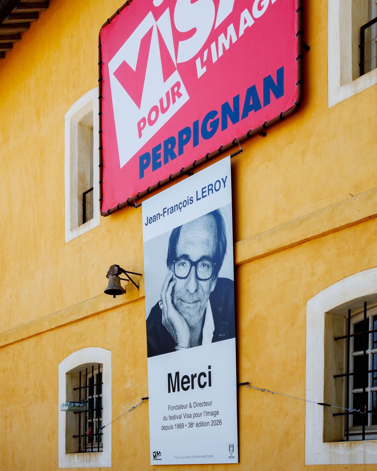 Yellow building facade displaying a tribute banner for Jean-Francois Leroy, founder of Visa Pour l'Image Perpignan.