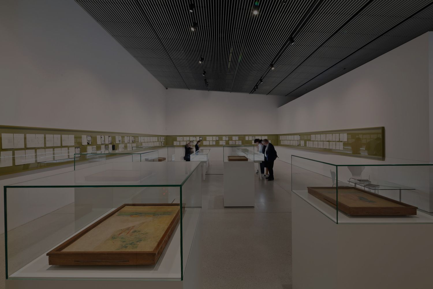 Modern museum gallery displaying artifacts in glass cases with visitors viewing exhibits along white walls.
