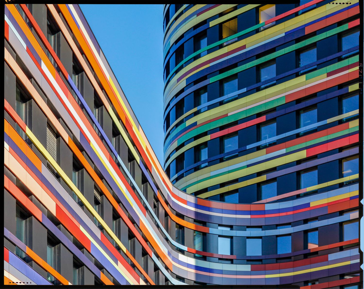 Colorful striped facade of curved modern buildings with vibrant horizontal bands under a blue sky.