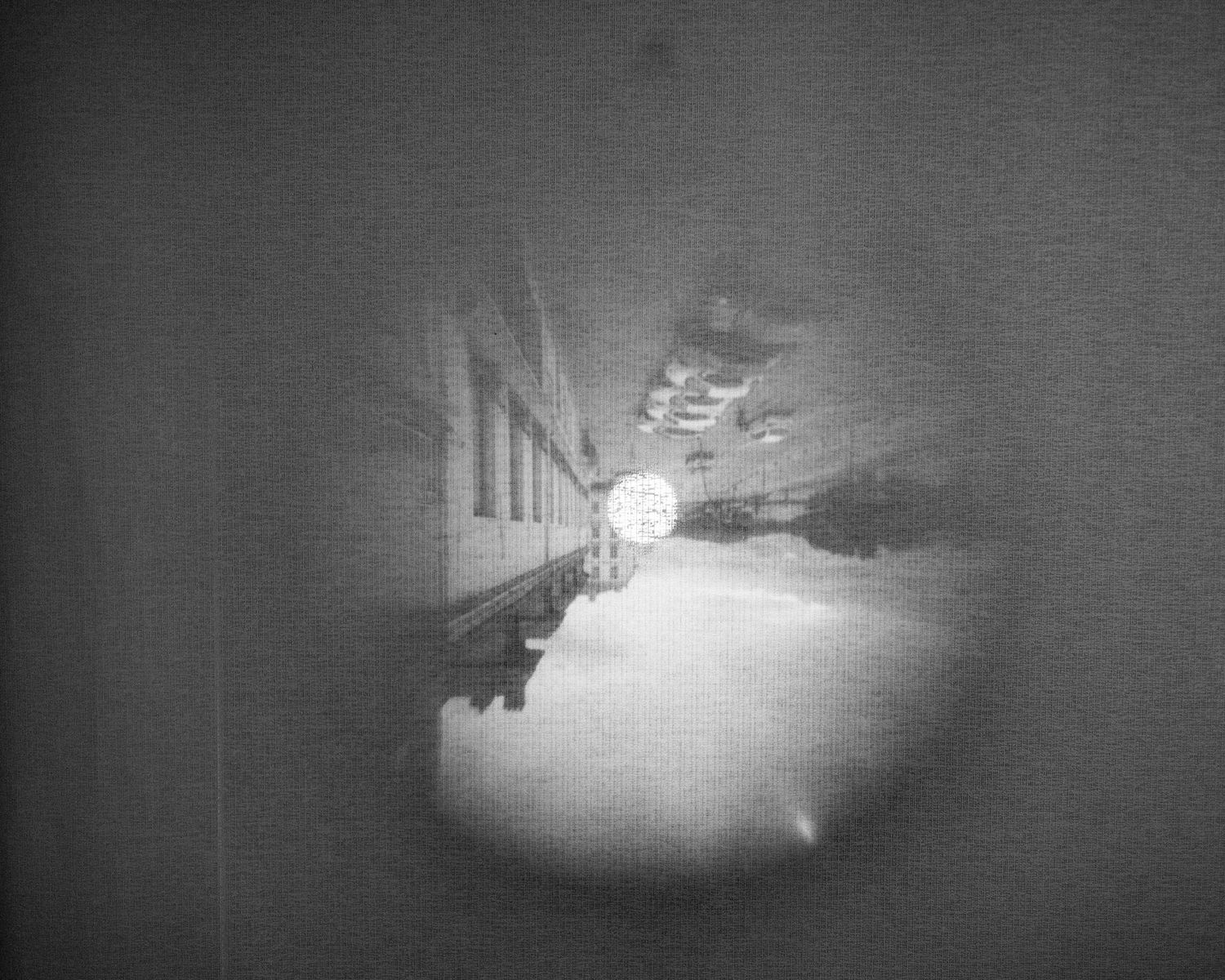 Black and white photo of a train tunnel with bright light at the end, captured through a circular vignette frame.