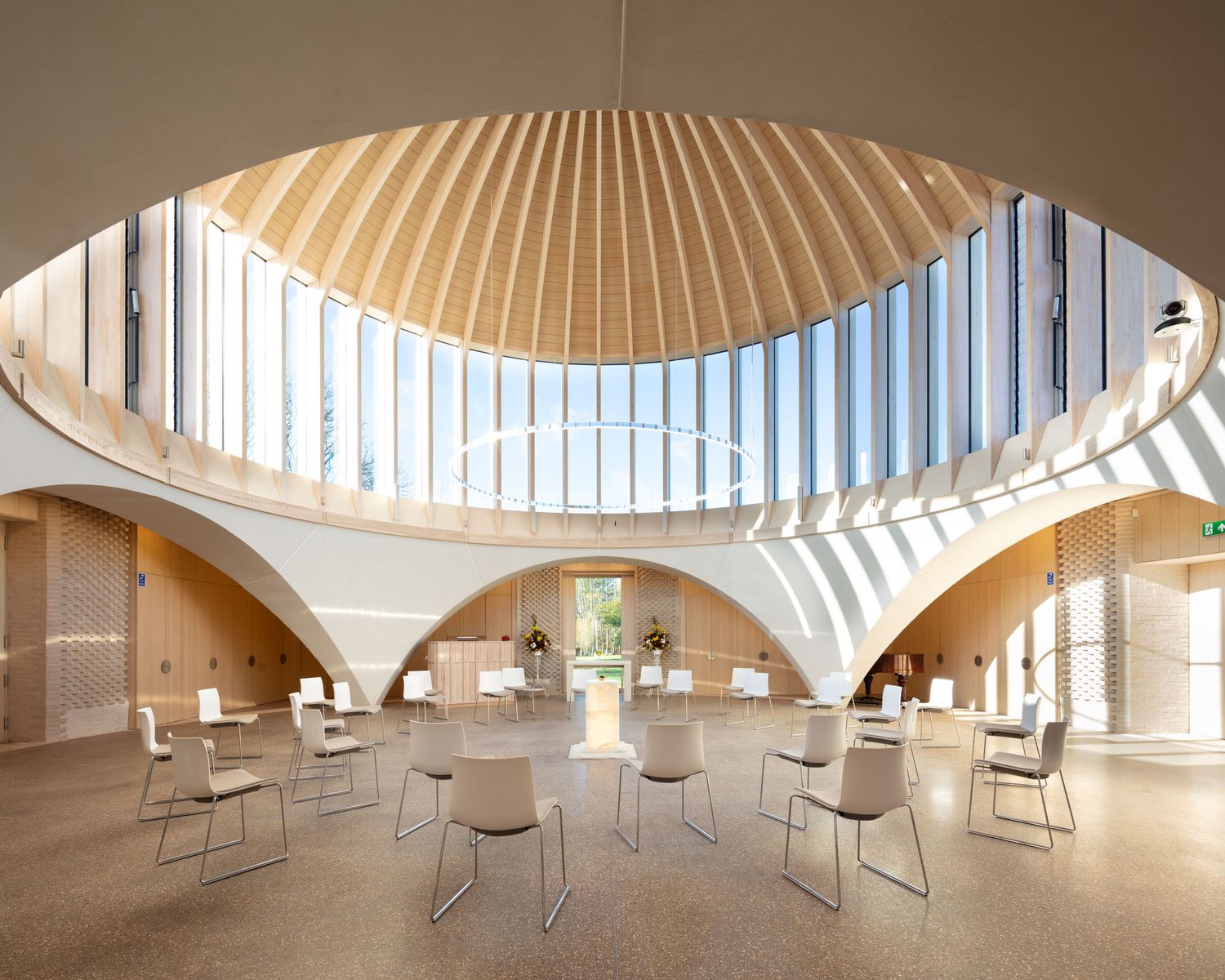 Stunning circular interior with curved wooden ceiling ribs, arched windows, and chairs arranged in a bright rotunda space.