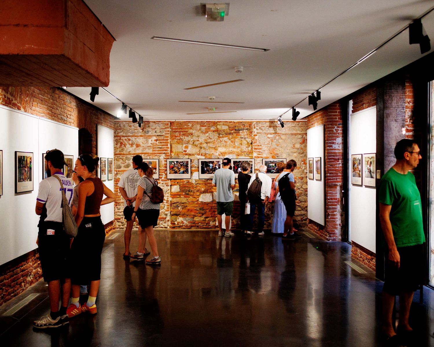 Visitors browsing photojournalism exhibition in a gallery with exposed brick walls and track lighting.