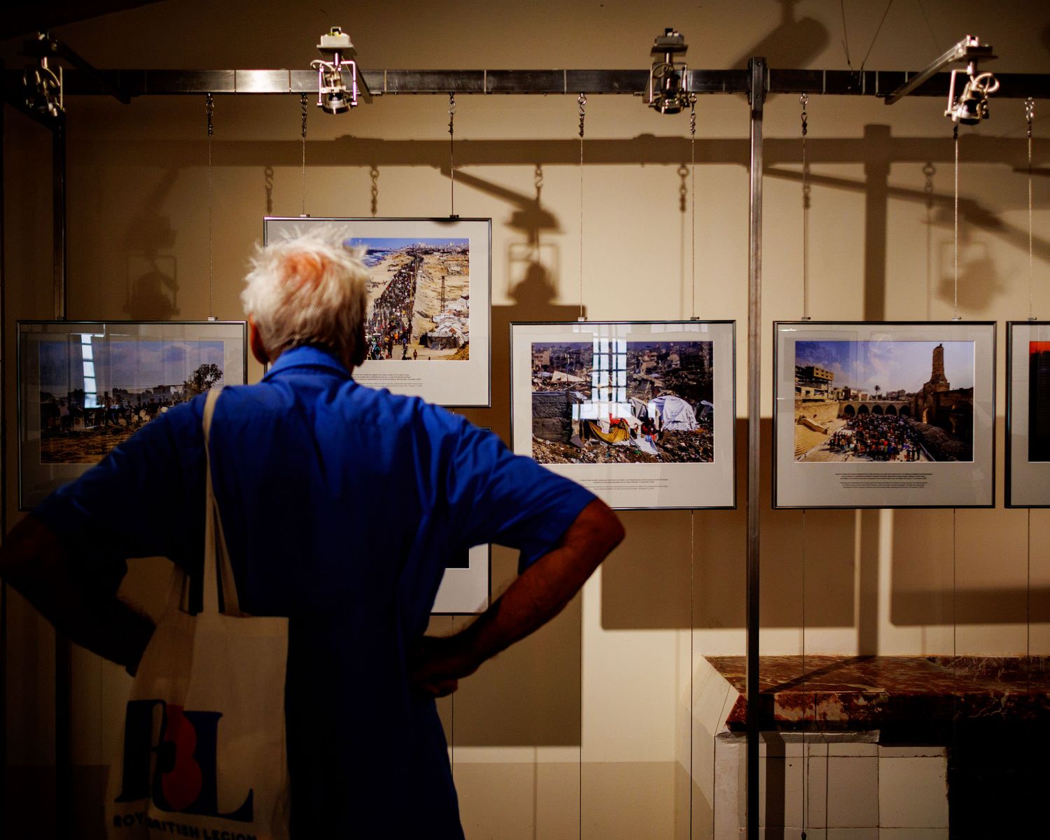 Man in blue shirt viewing framed color photographs displayed on a gallery exhibition stand indoors.