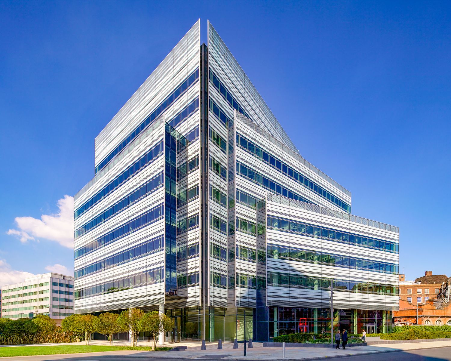 Modern glass and steel office building with blue reflective windows under a bright blue sky.