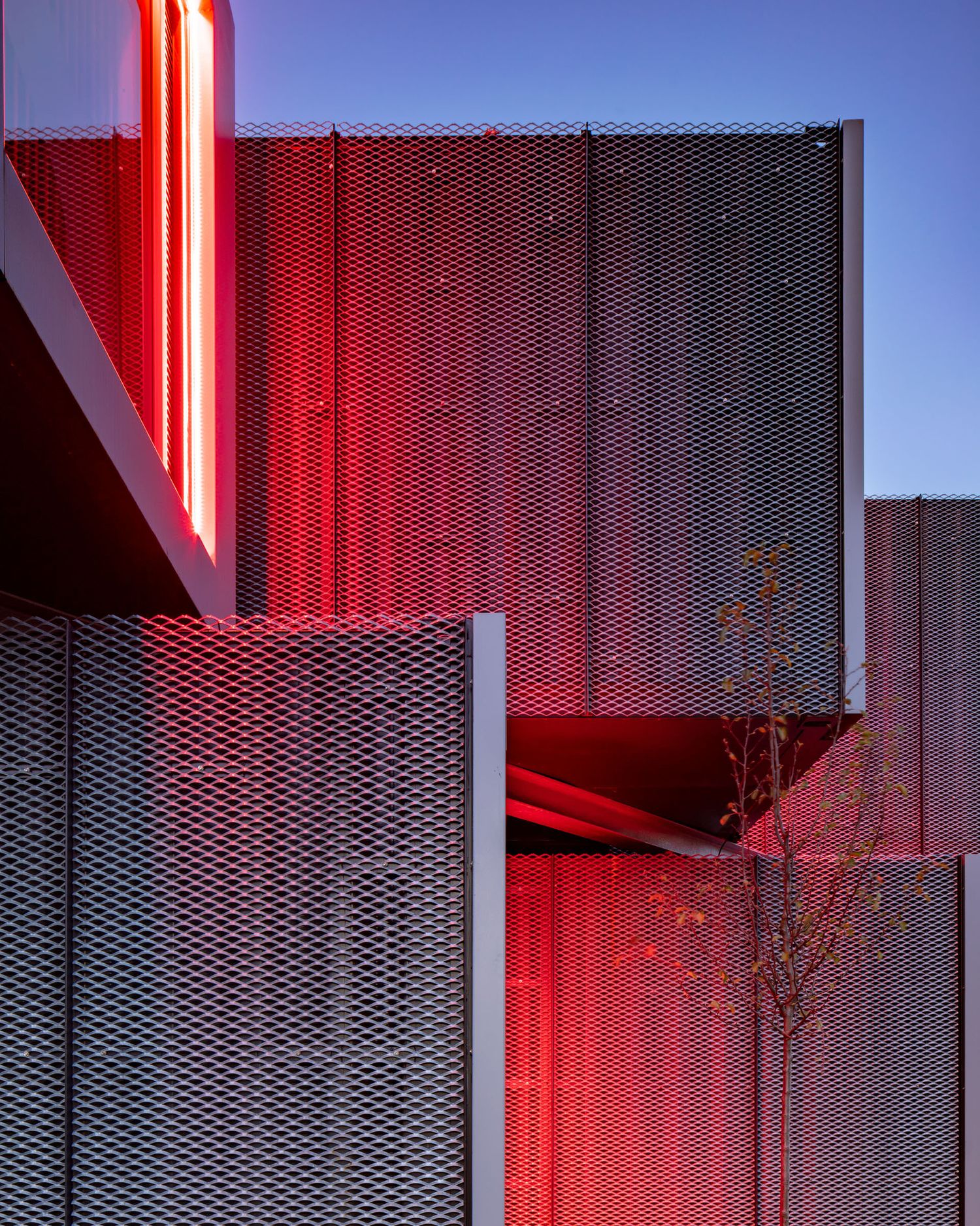 Bold red illuminated perforated metal facade panels on a contemporary building at dusk.