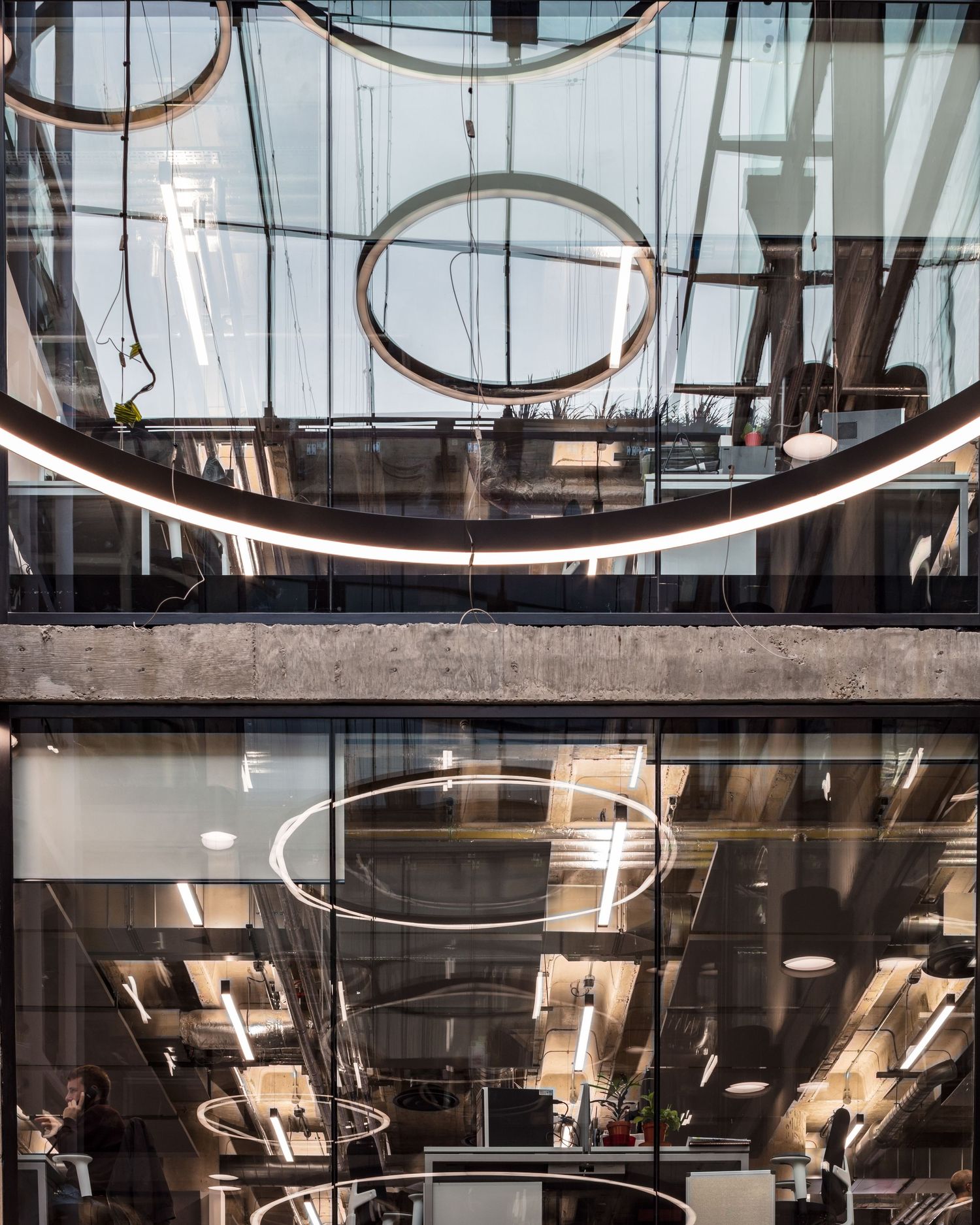 Modern office atrium with circular pendant lights, glass walls, and industrial ceiling details creating a striking architectural interior.