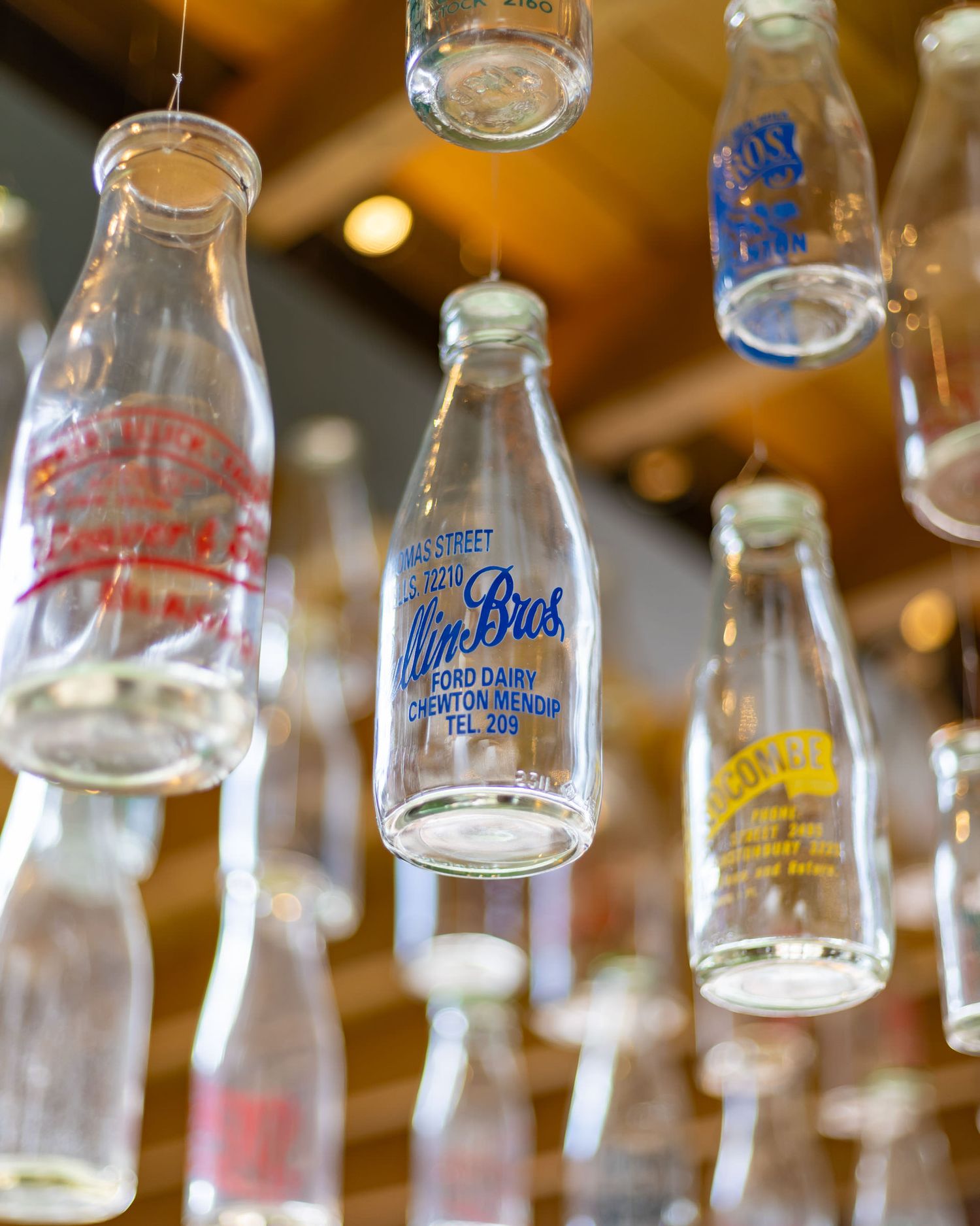 Vintage glass milk bottles hanging as decorative installation in a warmly lit interior space.