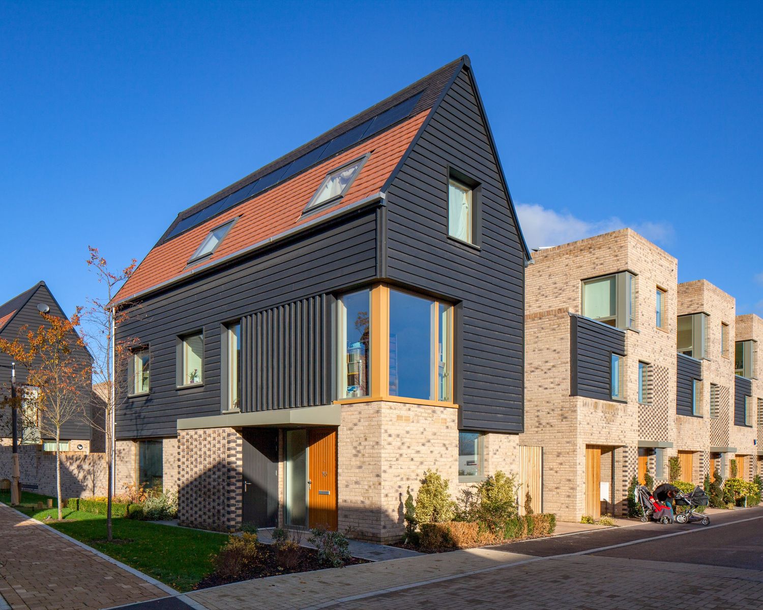 Modern residential homes featuring dark cladding, brick facades, and pitched roofs under a clear blue sky.