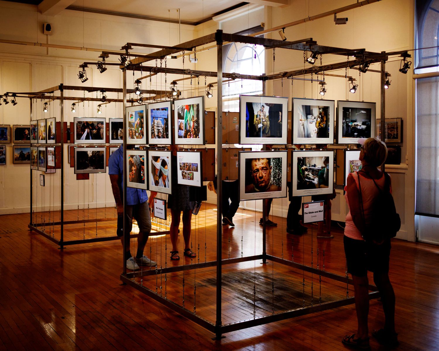 Visitors browsing colorful framed photographs displayed on metal grid structures in a well-lit gallery.