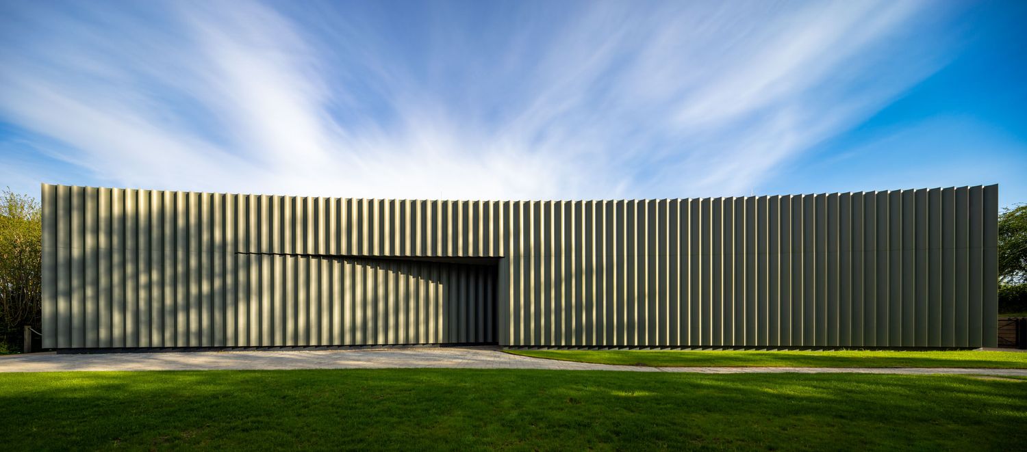 Modern minimalist building with vertical metal cladding facade set against a blue sky with green lawn foreground.