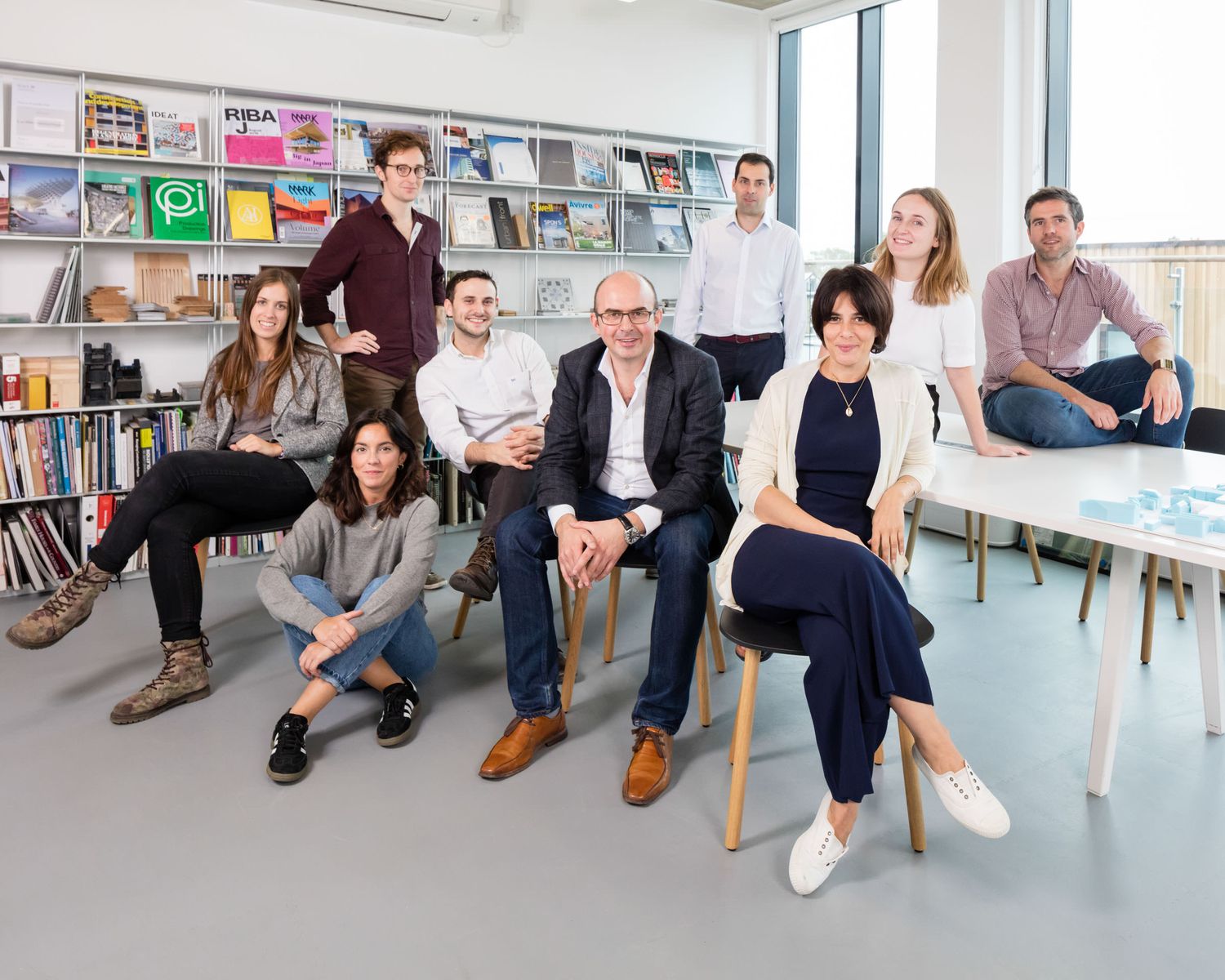 Group of ten architecture professionals posing together in a bright modern office library space.