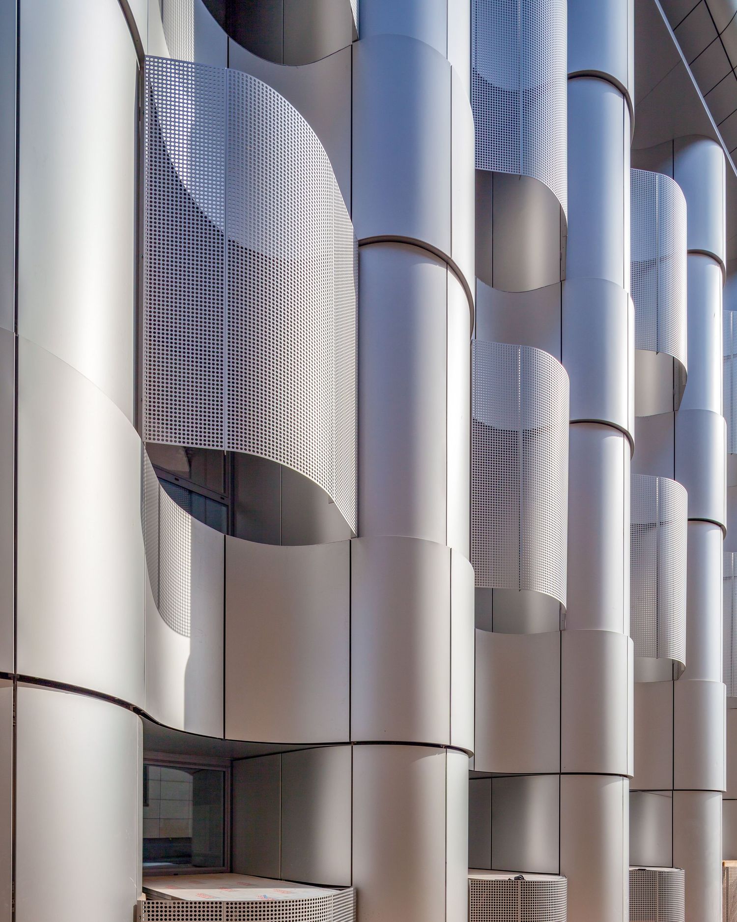 Modern building facade with curved silver cylindrical columns creating geometric patterns of light and shadow.