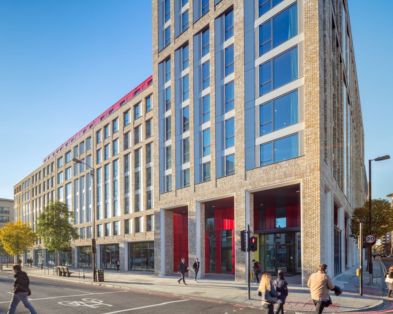 Modern multi-story commercial building with red accents, large glass windows, and pedestrians on a sunny urban street.