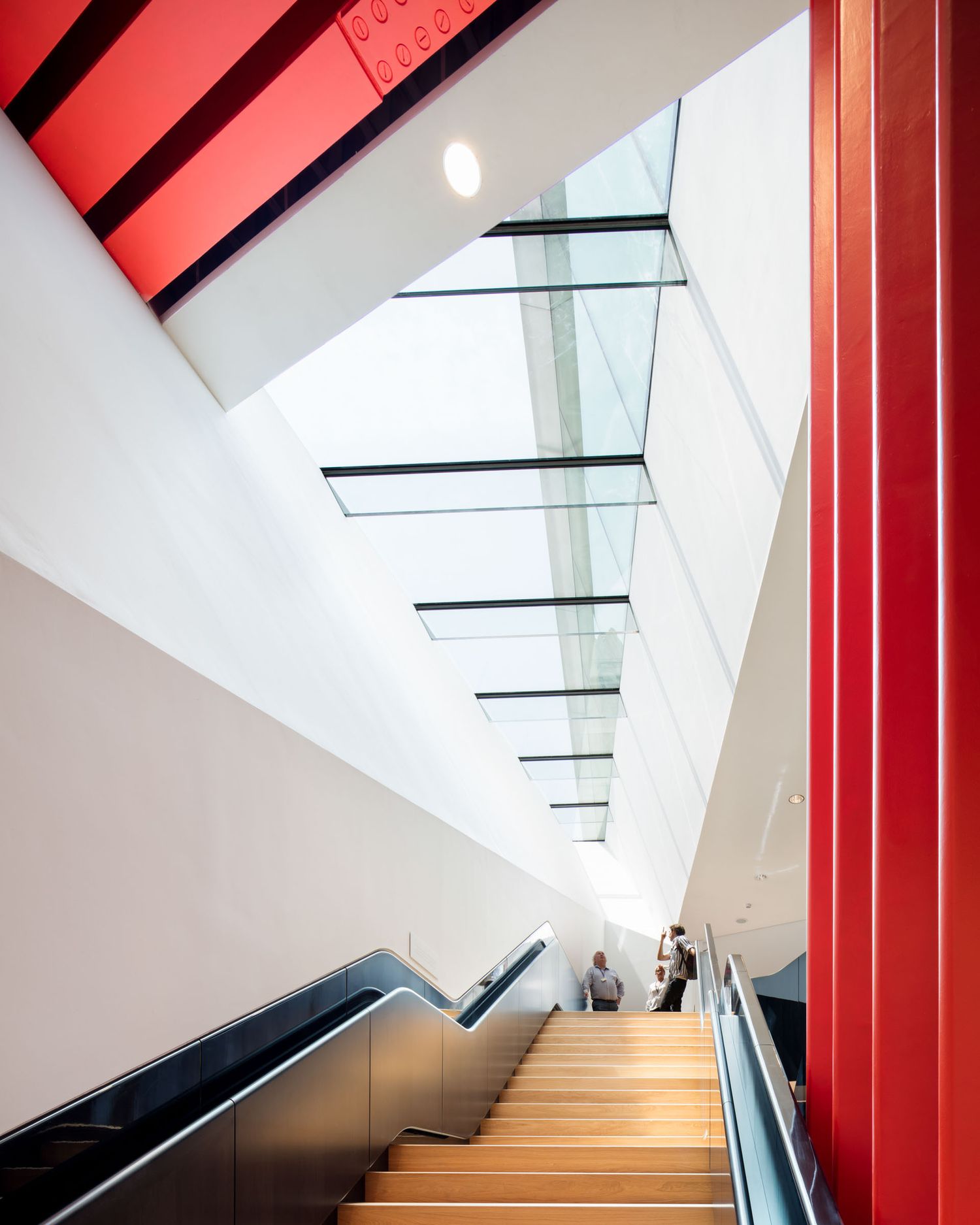 Bright modern staircase with red accent walls and angled skylights in a contemporary building.