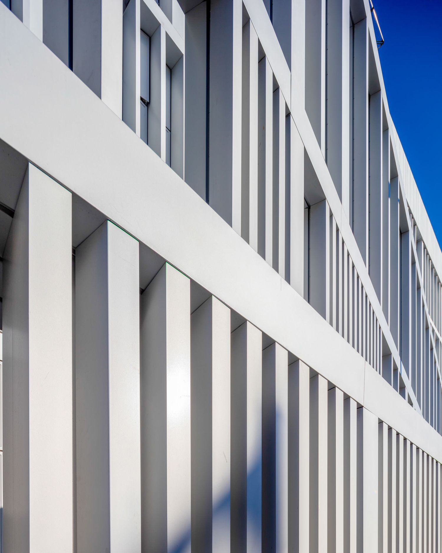 Modern white building facade with vertical fins and blue sky, showcasing clean architectural lines.