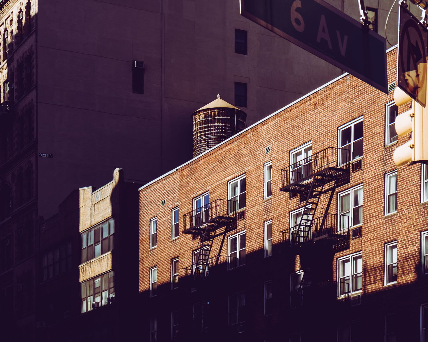 Brick apartment building with fire escapes and water tower in New York City near 6th Avenue.