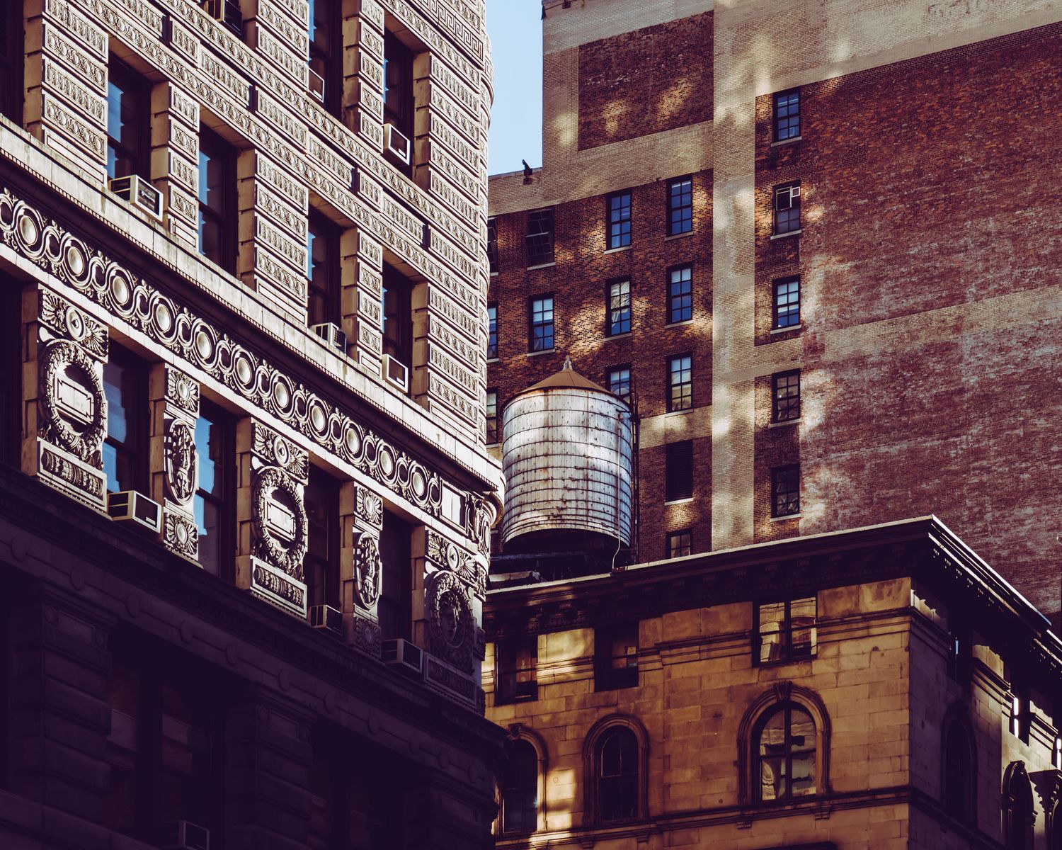 Historic brick buildings with ornate architectural details and a rooftop water tower in an urban cityscape.